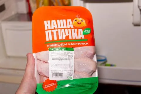 Raw chicken meat in plastic vacuum packaging held by hand in front of open Photos