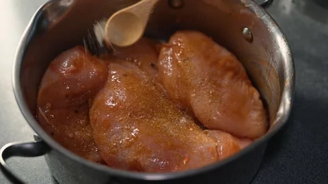 Raw chicken pieces are placed in a pot and coated with spices. A hand is seen Stock Footage 339097427