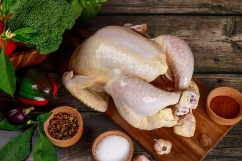 Raw chicken is presented on cutting board, along with spices that will be used Stock Photos