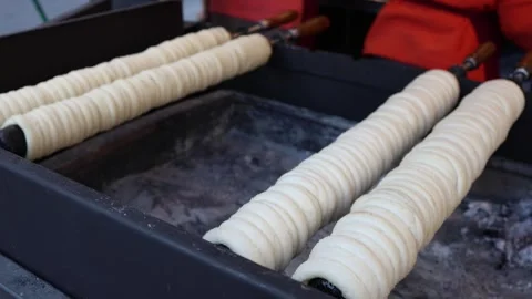 Raw chimney cake dough roasting on rolls over coals Stock Footage 331812168