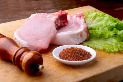 Raw chop on a rustic cutting board with salt, pepper and grinder for spices Stock Photos