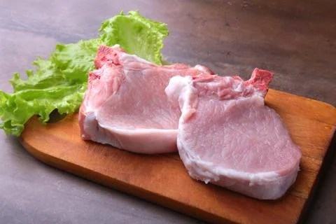 Raw chop on a rustic cutting board with salt, pepper and grinder for spices Stock Photos