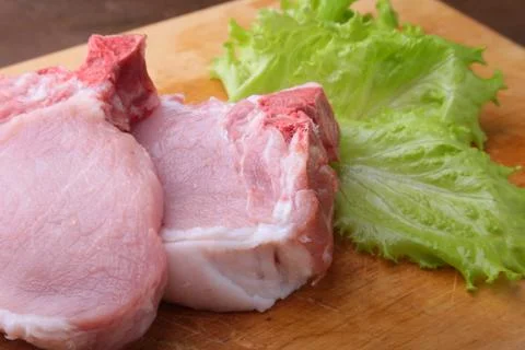 Raw chop on a rustic cutting board with salt, pepper and grinder for spices Stock Photos