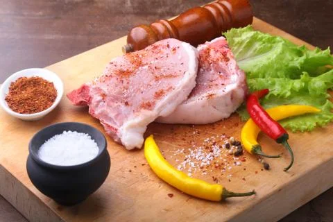 Raw chop on a rustic cutting board with salt, pepper and grinder for spices Stock Photos