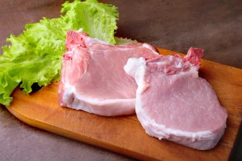 Raw chop on a rustic cutting board with salt, pepper and grinder for spices . Stock Photos