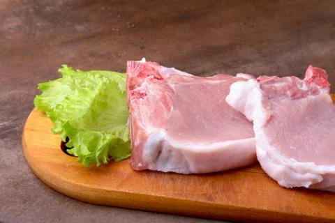 Raw chop on a rustic cutting board with salt, pepper and grinder for spices . Stock Photos