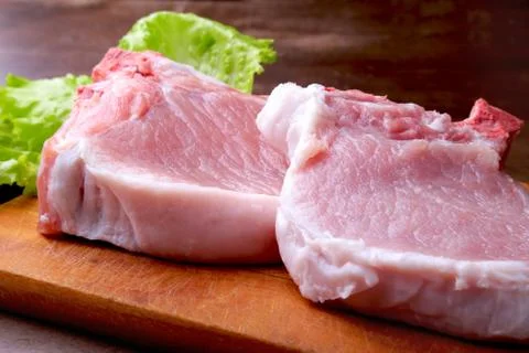 Raw chop on a rustic cutting board with salt, pepper and grinder for spices Stock Photos