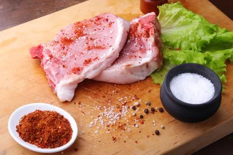 Raw chop on a rustic cutting board with salt, pepper and grinder for spices Stock Photos