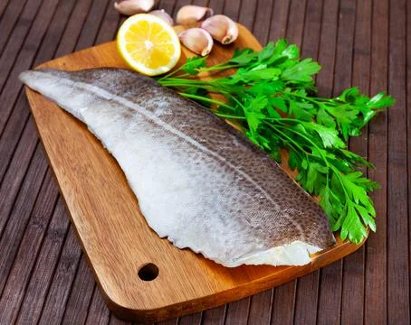 Raw cod fillet with garlic and lemon on wooden surface Stock Photos