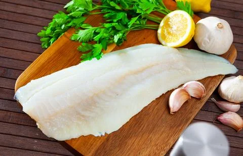 Raw cod fillet with garlic and lemon on wooden surface Stock Photos