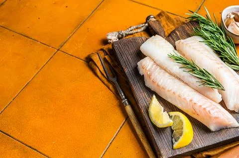 Raw cod fish fillets, codfish with rosemary on wooden board. Orange backgro.. 스톡 사진