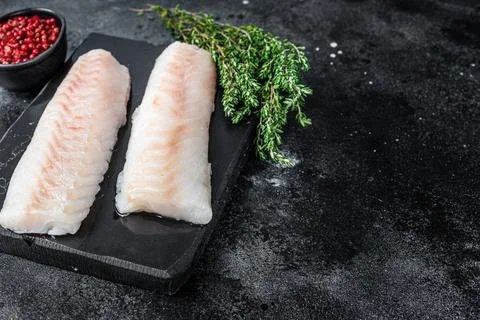 Raw cod loin fillet fish on marble board. Black background. Top view. Copy space Stock Photos