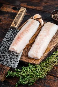Raw cod loin fillet steak on wooden board with butcher cleaver. Dark wooden Stock Photos