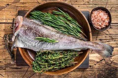 Raw cod or codfish fish in wooden plate with herbs. Wooden background. Top view Stock Photos