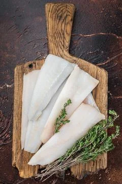 Raw cod or hake fillets with thyme on wooden board and pepper on dark textu.. 스톡 사진