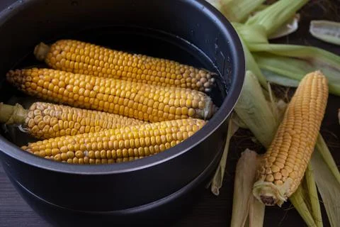 Raw corn in a saucepan with water on the table Stock Photos