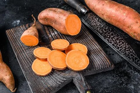 Raw cut batata Sweet potato on Wooden cutting board. Black background. Top view Stock Photos
