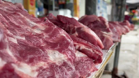 Raw cuts of red meat are arranged across a vendor table, with the butcher 動画素材 329298466