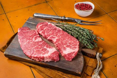 Raw Denver beef meat Steak with pink pepper and thyme. Orange background. Top Stock Photos