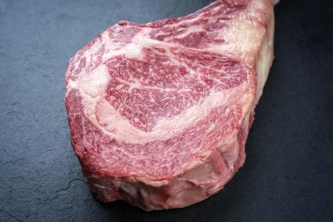 Raw dry aged wagyu tomahawk beef steak offered as close-up on black board Stock Photos