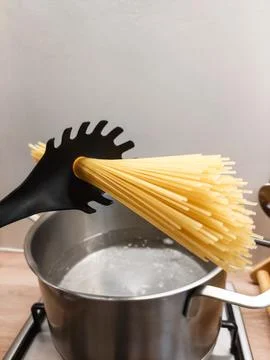 Raw Dry Spaghetti Pasta Held by Black Pasta Spoon Over Stainless Steel Pot 스톡 사진