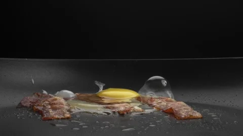 Raw egg is broken and falls on top of three slices of bacon hot frying pan Stock Footage 123577632