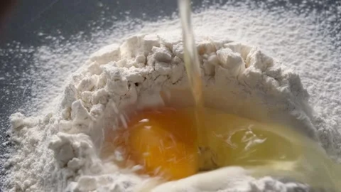 A raw egg is broken into a pile of flour, it slowly falls, the ingredients for Stock Footage 246491671