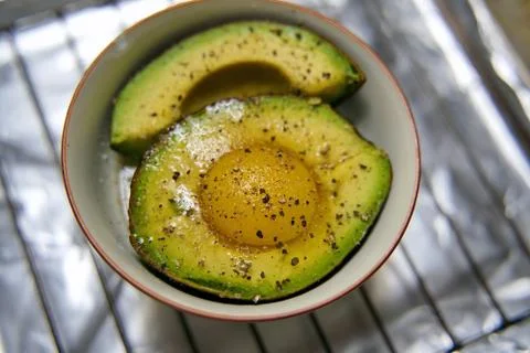 Raw egg cracked into a split avocado ready to be baked with salt and pepper f Stock Photos