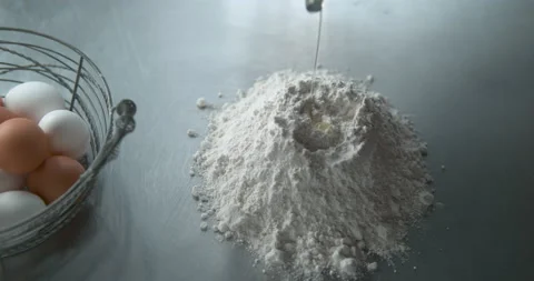 Raw egg dropped into a pile of flour on a metal kitchen counter next to a metal Video stock 199455755