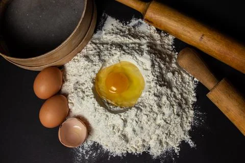 Raw egg in flour on a black background. Dough preparation. Stock Photos