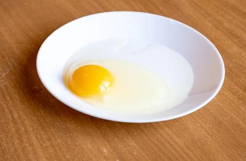 Raw egg in a white plate on the table. Stock Photos