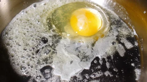 Raw egg yoke dropping in hot silver frying pan with butter fast to slow motion Stock Footage 153194134