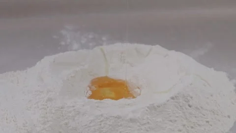 Raw egg yolk falling into pile of flour making hole. Stock Footage 313972978