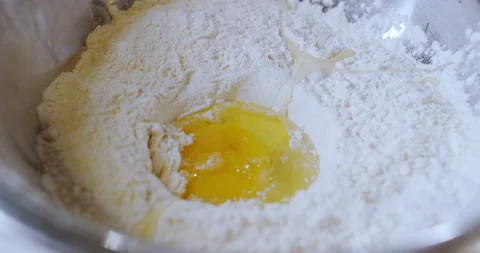 A raw egg yolk falls into a tray, a plate full of wheat flour. Slow motion. Stock Footage 146479973