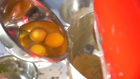 Raw eggs are poured into an electric mixer for whipping. Preparation of cake Stock Footage 208046003