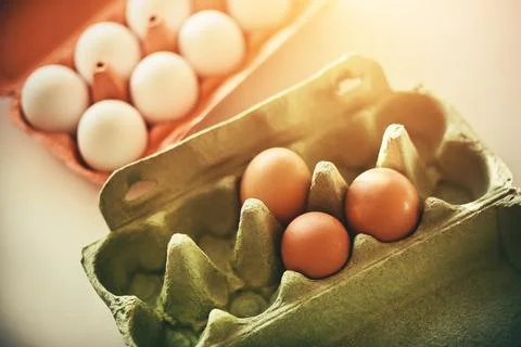 Raw eggs in white and brown shells lie in red and green cardboard packages, s Stock Photos
