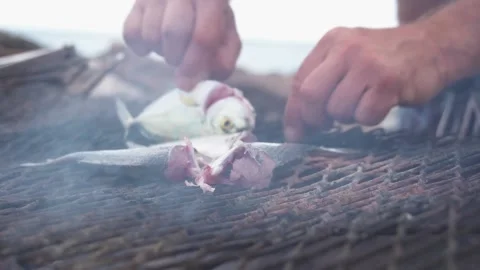 Raw fish cooked on an open grill with no cooking utensils. Man using bare hands. Stock Footage 136258620