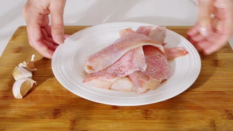 Raw fish fillets and garlic cloves placed on a white plate and wooden board. Video stock 331145913