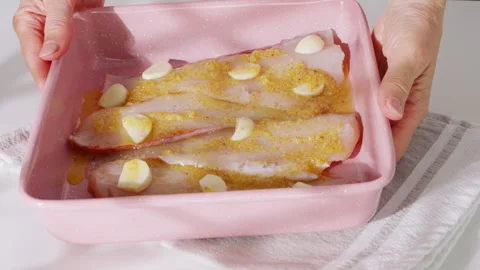 Raw fish fillets with garlic cloves in a pink baking dish. Stock Footage 308181888