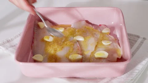 Raw fish fillets with garlic cloves in a pink baking dish. 库存影片 331146107