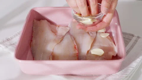 Raw fish fillets with garlic cloves in a pink baking dish. Stock Footage 331146269