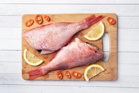 Raw fish perch without a head with lemon slices and red hot chili peppers o.. Foto stock