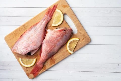 Raw fish perch without a head with lemon slices and red hot chili peppers o.. Foto stock