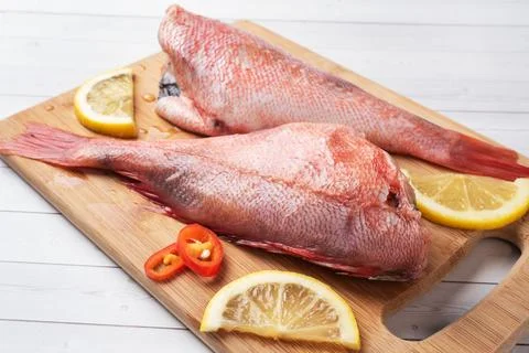 Raw fish perch without a head with lemon slices and red hot chili peppers o.. Foto stock