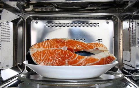 Raw fish in plate defrosting using microwave oven in close up Stock Photos
