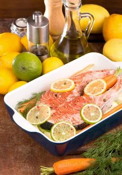 Raw fish is ready for baking. Salmon steak. Red fish and sliced lemons on whi Stock Photos