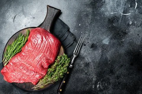 Raw flank beef steak, uncooked meat with herbs. Black background. Top view. Copy Stock Photos