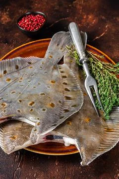 Raw flounder or plaice on rustic plate with herbs. Dark background. Top view Stock Photos