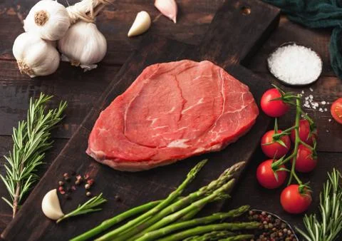 Raw fresh beef braising steak on chopping board with garlic, asparagus Stock Photos