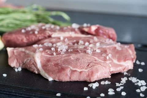 Raw fresh beef steak with salt and herbs on a black cutting board Stock Photos
